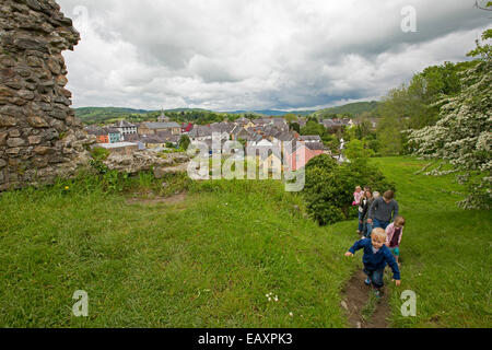 View of Welsh town of Llandovery from hilltop ruins of castle with family walking to summit on narrow track through grass Stock Photo