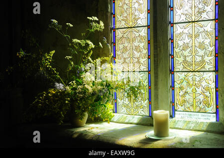 Sunlight through a stained glass window lights a floral display in the Church of St. Peter, Long Bredy, Dorset, England Stock Photo