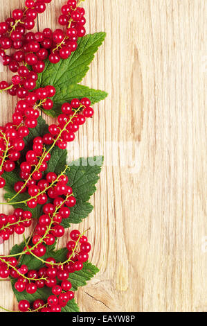 Red currants and green leaves on wooden background Stock Photo