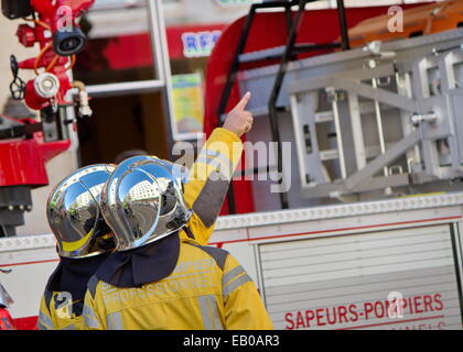 Two firefighters wearing helmets discussing next to fire truck, Geneva, Switzerland Stock Photo