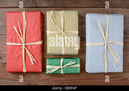 High angle shot of a four presents wrapped with colorful tissue paper. The gifts are tied with raffia and are laying on a rustic Stock Photo