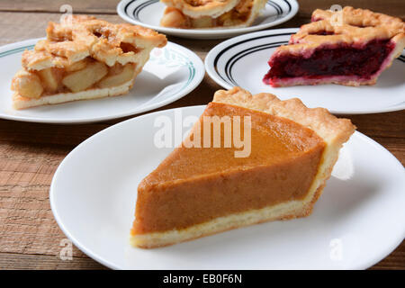 Closeup of four slices of pie on dessert plates. Focus is on the front slice of pumpkin pie.  back plates have apple and cherry Stock Photo