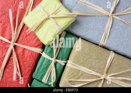 High angle closeup shot of a group of Christmas presents wrapped with colorful tissue paper. The gifts are tied with raffia. Stock Photo