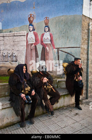 Men wearing traditional old Mammuthones mask during a break near mural painting, Mamoiada carnival, Sardinia, Italy Stock Photo