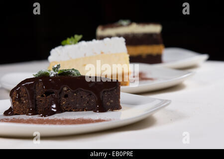 Assorted desserts in a bakery or restaurant with individual slices of rich chocolate tart, layer cake and cheesecake served on plates at table. Stock Photo