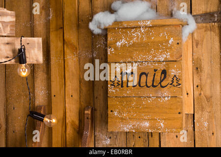 Old wooden handmade mailbox mounted on the exterior wall of a rustic timber house, decorated with Christmas lights, in a snowy d Stock Photo