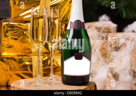 Celebrating with luxury champagne with two full flutes standing alongside a bottle with a blank label and elegant gift-wrapped boxes in gold paper for Christmas, New Year or an anniversary. Stock Photo
