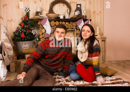 Portrait of Couple Wearing Sweaters Sitting on Floor inside Log Cabin in Winter Stock Photo