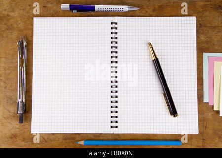 pens, pencils and other office accessories near cheked notebook on wood texture Stock Photo
