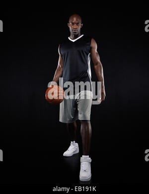 Portrait of confident young basketball player over black background. African young man in sportswear holding a basketball. Stock Photo