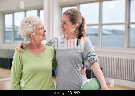 Portrait of happy senior woman with her personal trainer at gym. Two women standing together looking at each other. Stock Photo