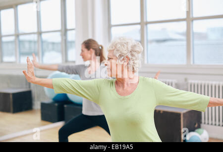 Two women doing stretching and yoga workout at gym. Female trainer in background with senior woman in front during training. Stock Photo