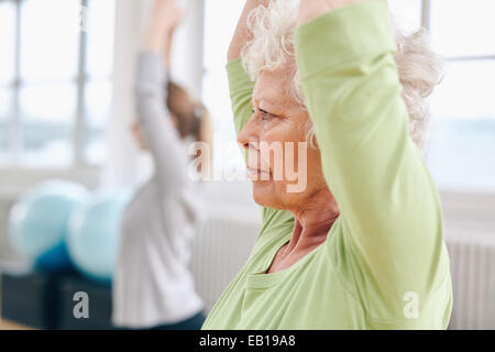 Close-up image of senior woman practicing yoga at gym. Active senior woman exercising at health club with female trainer in back Stock Photo