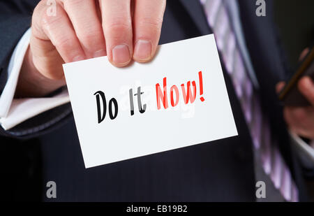 A businessman holding a business card with the words,  Do It Now, written on it. Stock Photo