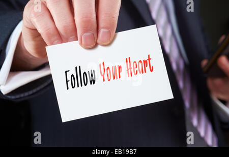 A businessman holding a business card with the words, Follow Your Heart, written on it. Stock Photo