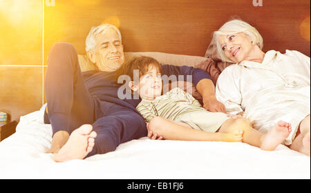 Happy grandparents with grandson laying on bed in a bedroom Stock Photo
