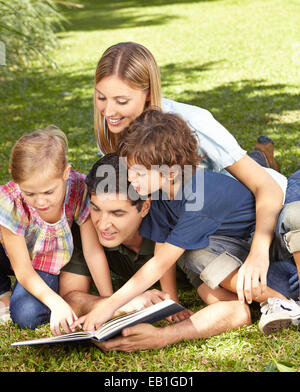 Two children reading book with family in a green garden Stock Photo