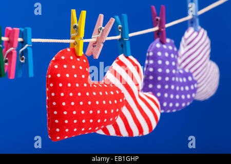 hearts hanging on a clothesline with clothespins, focus on red. Blue background Stock Photo