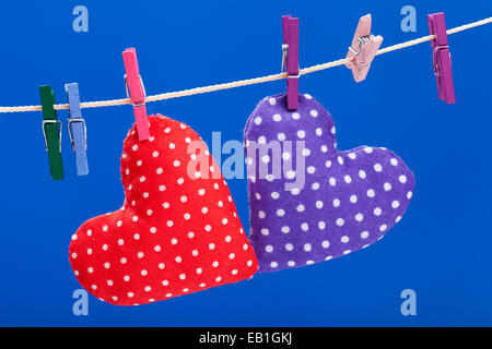two hearts hanging on a clothesline with clothespins, blue background Stock Photo