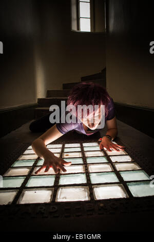 A young teenage girl woman trapped confined in a prison cell type location with light streaming through a barred window