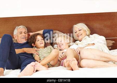 Grandparents tickling two grandchildren on bed in bedroom Stock Photo