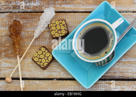 Black coffee, chocolates and sugar sticks on rustic wooden surface Stock Photo