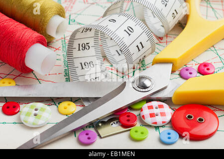 Sewing items: buttons, colorful fabrics, scissors, measuring tape, thimble, spools of thread on sewing pattern Stock Photo