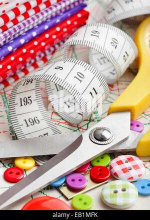 Sewing items: buttons, colorful fabrics, scissors, measuring tape, thimble, spools of thread on sewing pattern Stock Photo