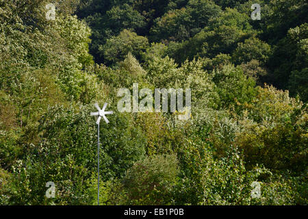 Small wind turbine rotating with wind blowing trees behind, Wales, UK Stock Photo
