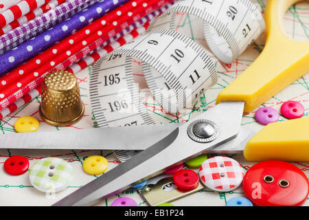 Sewing items: buttons, colorful fabrics, scissors, measuring tape, thimble, spools of thread on sewing pattern Stock Photo
