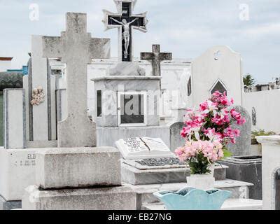 Marble and stone Christian graves with crosses and grave offering of bright pink flowers in the Panteon de San Roman cemetery, Campeche, Mexico. Stock Photo