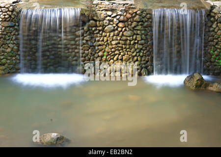 Two small waterfalls separated by a stone wall. Stock Photo