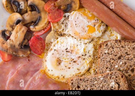 English breakfast with two fried eggs, two viennas, two slices of toast, three slices of fried ham and some fried mushrooms and Stock Photo