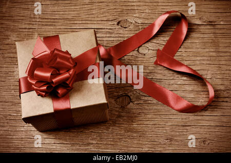 a gift box tied with red ribbon on a rustic wooden table and red ribbon forming a heart, with a retro effect Stock Photo