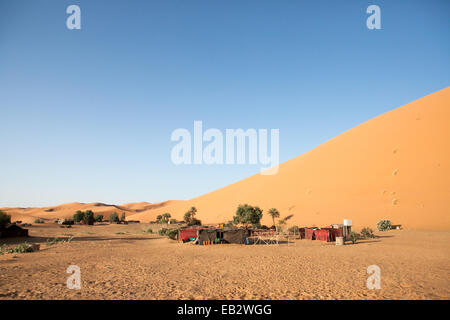 A small tented camp is visible near a sand dune in the Sahara desert. Stock Photo