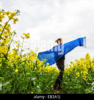 Woman holding wide blue scarf spinning in rapeseed field Stock Photo