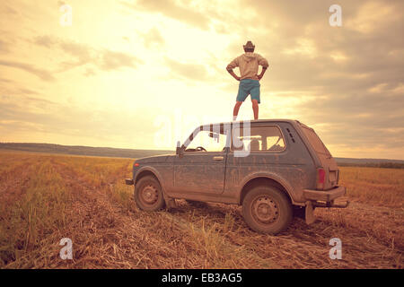 Mari man standing on car roof in rural field Stock Photo