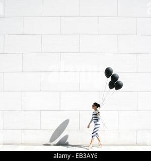 Woman walking past a wall carrying a bunch of balloons Stock Photo