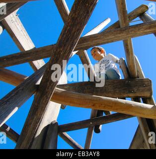 Low angle view of boy playing on a wooden climbing frame in a playground Stock Photo