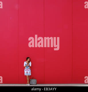Woman standing next to her handbag in front of a red wall text messaging Stock Photo