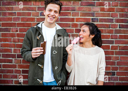 Caucasian couple eating ice cream near red brick wall Stock Photo