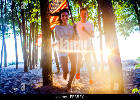 Caucasian couple carrying American flag in trees on beach Stock Photo