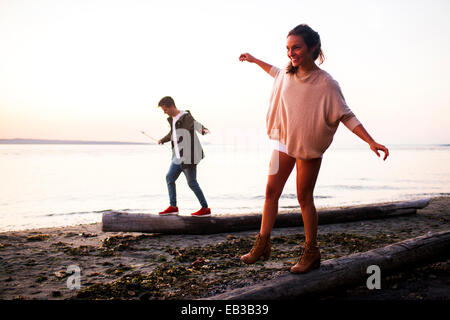 Caucasian couple walking on logs on beach Stock Photo