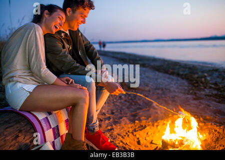 Caucasian couple roasting marshmallows on fire at beach Stock Photo