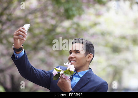 Man in suit taking cell phone selfie while holding flowers Stock Photo