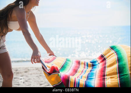 Caucasian woman spreading blanket on beach Stock Photo