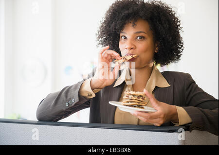 Businesswoman eating stack of cookies in cubicle Stock Photo