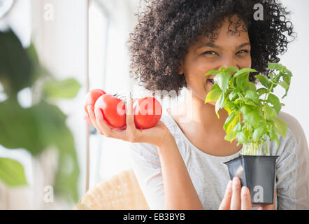 Smiling woman with tomatoes smelling plant Stock Photo