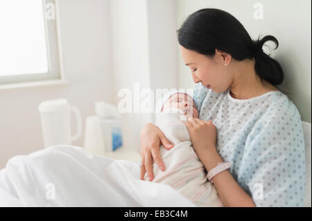 Asian mother holding newborn baby in hospital bed Stock Photo