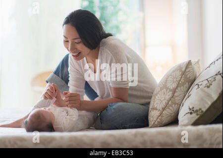 Asian mother playing with baby on bed Stock Photo